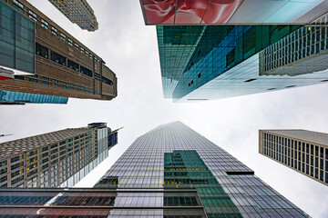 Looking up at modern skyscrapers in Midtown Manhattan forming geometric perspective against cloudy sky, New York City
