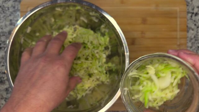 overhead view of hands packing shredded cabbage into glass jar for fermentation