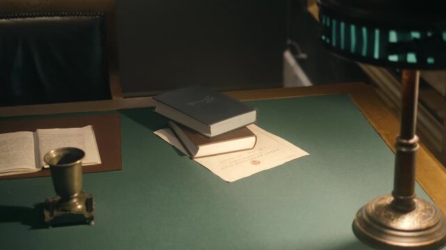 An old-fashioned desk with a lamp, books, a rotary phone, a folder with documents and pens for writing. A leather chair is nearby. Shot in motion