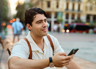 Young man enjoys sunny day while using smartphone in urban setting, highlighting his joy and...