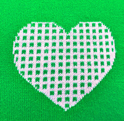 heart on a green background. knitted fabric with a pattern. The scheme for knitting and needlework in the shape of a heart. sweater print close up, texture. High quality photo
