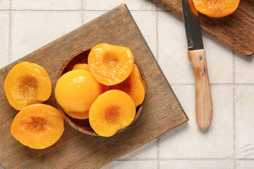 Wooden bowl and cutting board with sweet canned peaches on white tile background