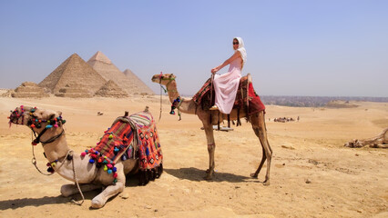 A joyful traveler rides a camel in the Egyptian desert with the iconic Giza pyramids in the background, capturing the perfect vacation moment.