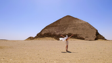 A woman enjoying a peaceful vacation moment in Egypt, standing in the desert with arms raised in front of an ancient pyramid, capturing the spirit of travel and exploration.