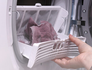 close up female hand taking lint out from dirty air filter of dryer machine after drying. cleaning Dirty filter. hair, wool from the filter in hand. Front Load Tumble Laundry electric Dryer Machine.