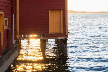 Golden sunset light reflecting on sea water under traditional red wooden Norwegian rorbu fisherman house on stilts in coastal Norway