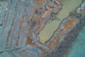 Stagnant toxic water pond in abandoned clay quarry with eroded grey earth, environmental pollution background, aerial top down drone shot