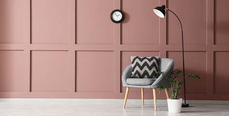Comfortable grey armchair with soft pillow and floor lamp near brown wall in living room