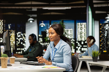 Black female works on researching and documenting reports after hours, data updates and business enterprise, after hours work in a dark office. Finance targets and project development.
