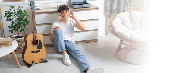 Handsome young man in headphones with record player listening to music at home