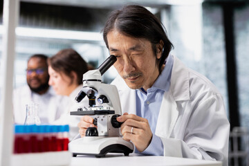 Nanotechnology researcher using microscope to evaluate cellular structures in lab. Research facility expert observes medical tissue through magnification tool at laboratory bench workstation