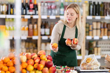 Young woman seller weighs apples in plastic bag in grocery store