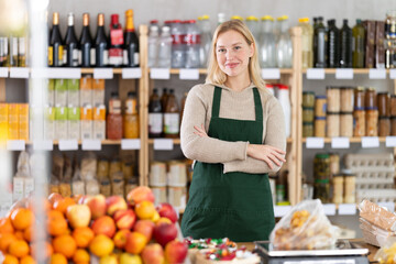 Young female seller in apron standing at counter in grocery store