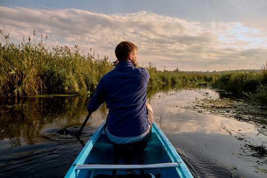 Man kayaking through calm river at sunrise