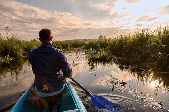 Man kayaking through calm river at sunrise