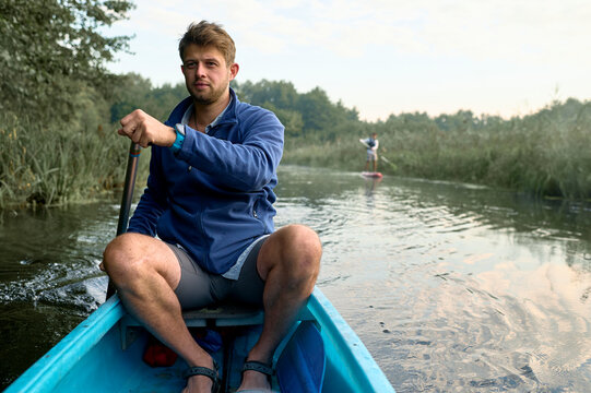 Man paddling kayak on river with paddle boarder in background
