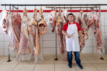 Butcher holding knife in front of hanging carcass at small butchery