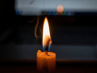 A vibrant candle flame casts a warm glow in a dimly lit environment with a wisp of smoke