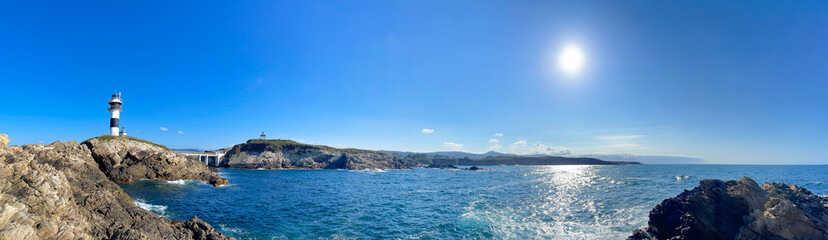 Panoramic view of the black and white lighthouse standing on a rocky cliff by the deep blue sea under a clear sky, Isla Pancha, Ribadeo, Galicia, Spain, panorama