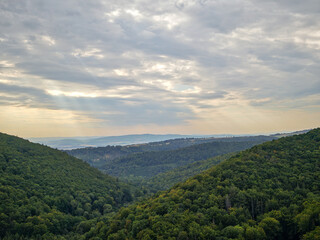 Naklejka premium Panoramic scenic view of green forested hills and valleys under a dramatic cloudy sky.