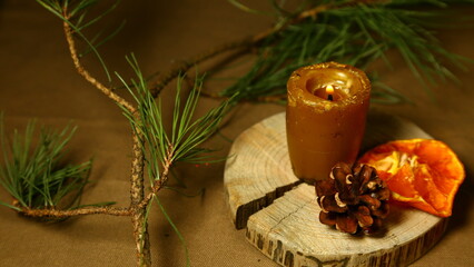 Burning Christmas wax candle on wooden candlestick near natural cone, dried orange on table with green natural fir branch. Home cozy aromatherapy relax eco ornament. Closeup