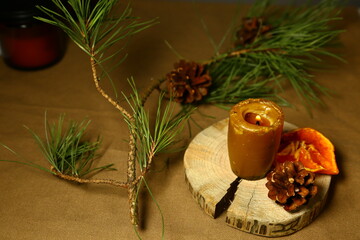 Burning Christmas wax candle on wooden candlestick near natural cone, dried orange on table with green natural fir branch. Home cozy aromatherapy relax eco ornament. Closeup
