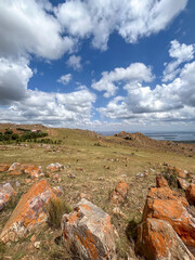Wide panoramic view of orange volcanic rocks and boulders in the Rwandan highlands overlooking a lake.