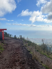 View from the top of Mount Vesuvius overlooking the sea and coastal city through a path with fence.