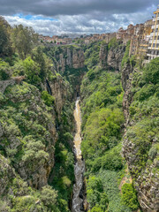 Vertical view into the deep and narrow Rhumel River gorge with steep cliffs and city buildings on the edge.