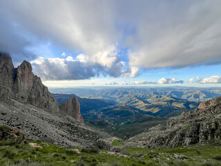 Panoramic view of steep rocky mountains and deep green valleys under a dramatic cloudy sky in Algeria.
