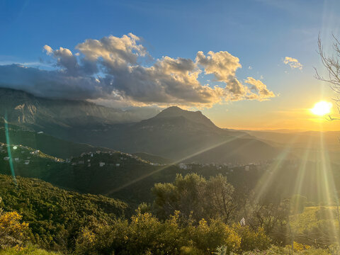 Golden sunset over the mountains of Kabylie in Algeria with strong lens flare and sunlight hitting the green hills.