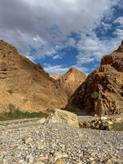 Deep rocky canyon gorge with high steep cliffs and a dry pebble riverbed in the Sahara region.