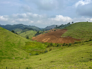 Panoramic landscape of terraced Rwandan hills with a large group of people working on tilled red soil in a rural village.