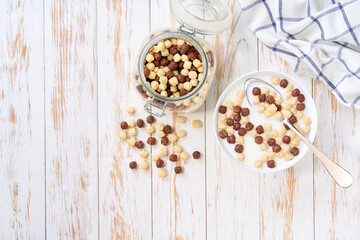 bowl of tasty  corn balls and chocolate corn balls with milk on a light kitchen table. Copy space for text. Top view.