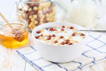 corn balls and chocolate corn balls in a bowl with milk and honey on a white wooden table.