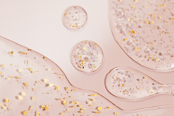 Serum fluid 24k gold gel facial cream smear, on beige pastel background. Beauty cosmetic product smudge, pure transparent lotion with gold particles, skin care jelly serum, top view Luxury moisturizer