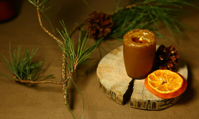 Burning Christmas wax candle on wooden candlestick near natural cone, dried orange on table with green natural fir branch. Home cozy aromatherapy relax eco ornament. Closeup