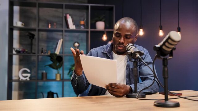 Black man podcasting, holding script and talking into professional studio microphone. Creating audio content for radio or digital media