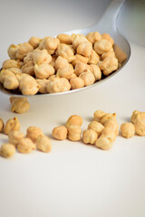Fototapeta premium Close-up of uncooked dried chickpeas in a metal spoon with soft focus on white background. Minimal ingredient detail.