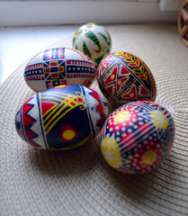Fototapeta premium A close-up, high-angle shot of a group of five colorful Ukrainian Pysanka Easter eggs with intricate traditional geometric and floral patterns, resting on a textured woven placemat with natural light.