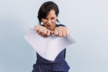 portrait of adult latina woman tearing blank paper with hands on blue background in Mexico Latin America, or hispanic senior brunette female 