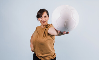 portrait of adult latina woman holding a soccer ball on blue background in Mexico Latin America, or hispanic senior brunette female in sportswear