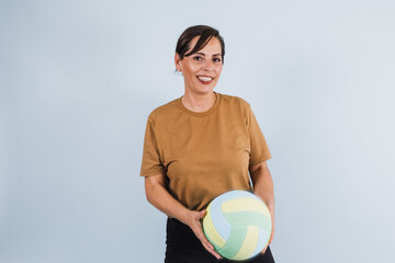 portrait of adult latina woman holding a volleyball ball on blue background in Mexico Latin America, or hispanic senior brunette female in sportswear