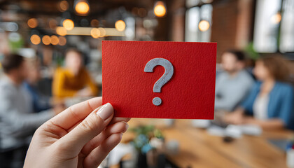 Hand holds card with red question mark sign at business meeting. Colleagues in office discuss project issues, seeking answers for teamwork problem. Uncertainty idea.