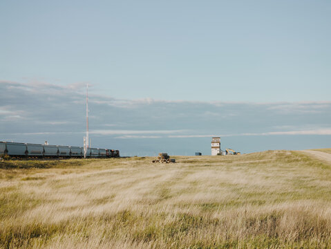 Freight train passing prairie field with old grain elevator