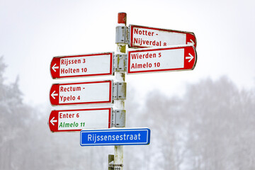 Blue street name sign of Rijssensestraat between Rijssen and Holten, The Netherlands with directions and distances to nearby towns and places. Graphic design signpost contrasted against Dutch hazy mis © Maarten Zeehandelaar
