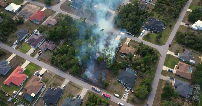 Aerial view of firefighters and fire trucks responding to vegetation fire burning dangerously close to houses in Florida residential neighborhood