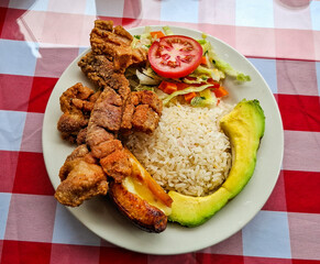Traditional Colombian lunch presented on a white plate with fried pork, rice, avocado, vegetable salad and ripe plantain, ideal for Latin gastronomy and culture.