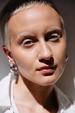 Person with short hair and earrings poses against a neutral backdrop