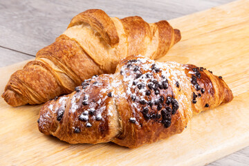 A French butter croissant and a sugar covered chocolate chip croissant on a wooden board
